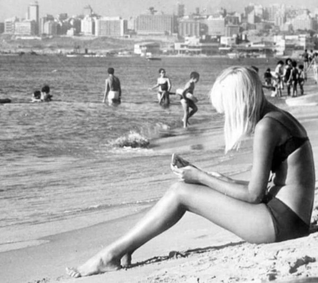 Woman sitting on a beach with the skyline of Beirut in the background – Lebanon, c. 1975. [1070 x 955]