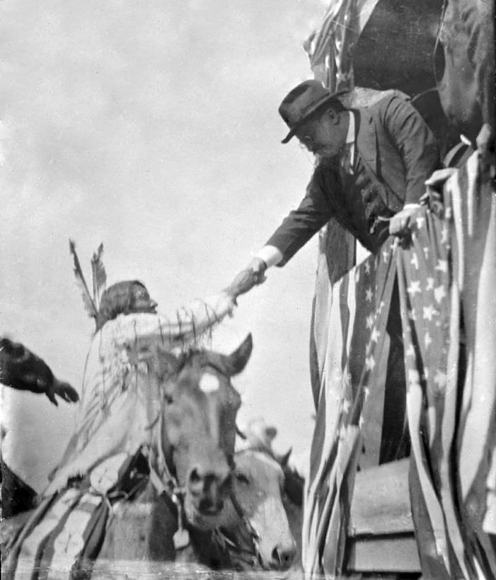 US President Theodore Roosevelt reaching from a traincar to shake hands with a native American man on horseback, 1912 (1051×900)