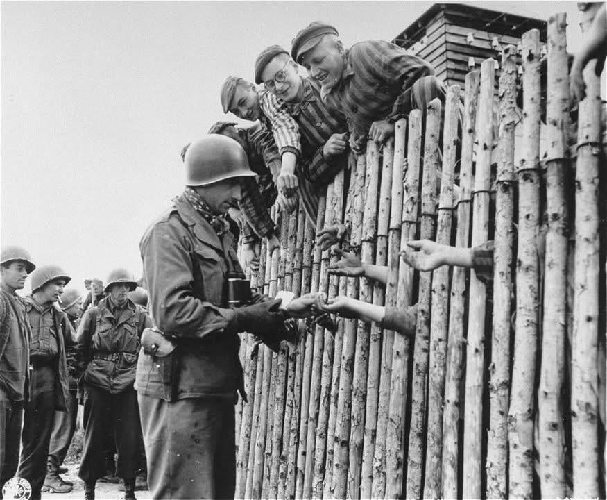 U.S. Army Corporal Larry Matinsk puts cigarettes into the extended hands of newly-liberated prisoners behind a stockade in the Munich-Allach Concentration Camp in Allach-Untermenzing, Germany, on April 30, 1945. [875×720]