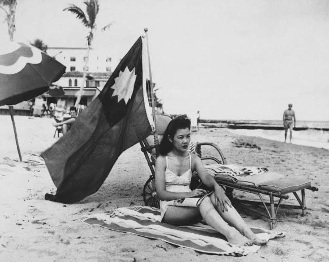 Ruth Lee, a Chinese restaurant hostess, displays a Chinese flag while sunbathing in Miami during her days off after the Pearl Harbor attack, to avoid being mistaken as Japanese, 1941. [1080×858]