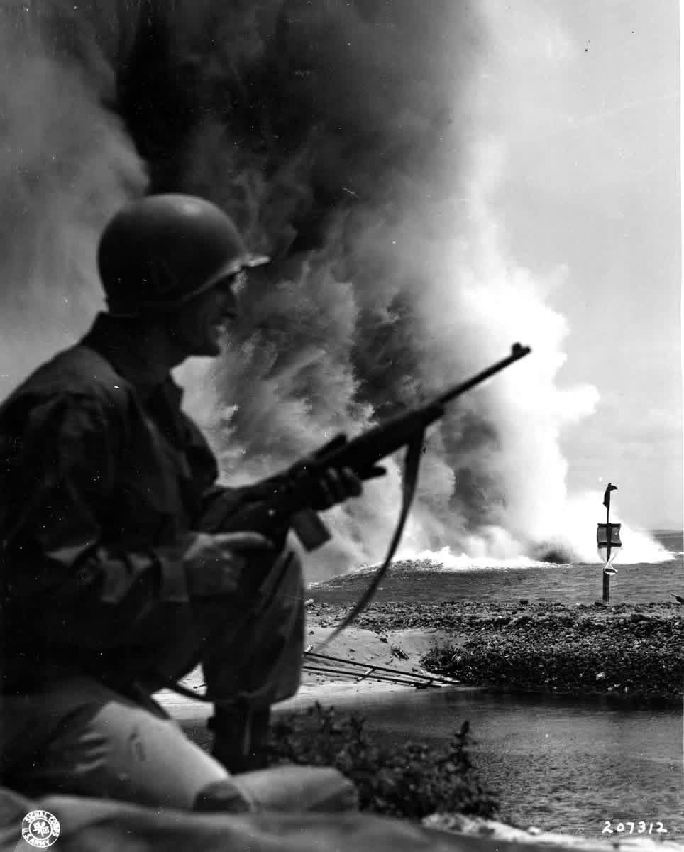 Framed by the silhouette of an alert soldier of the 77th Infantry Division, tons of water and coral are blown skyward by the force of a charge set to deepen a channel through a reef offshore, Okinawa. 24 April, 1945. [964×1200]