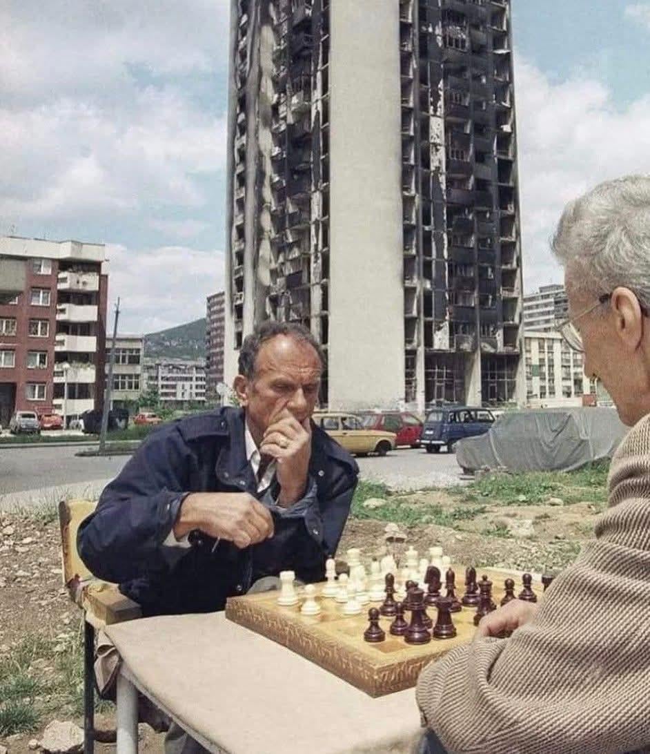 Two men having a chess match – near the burnt out ruin of an apartment bloc – in Hrasno, during the Siege of Sarajevo in the Bosnian War, c. 1994. [942 x 1092]