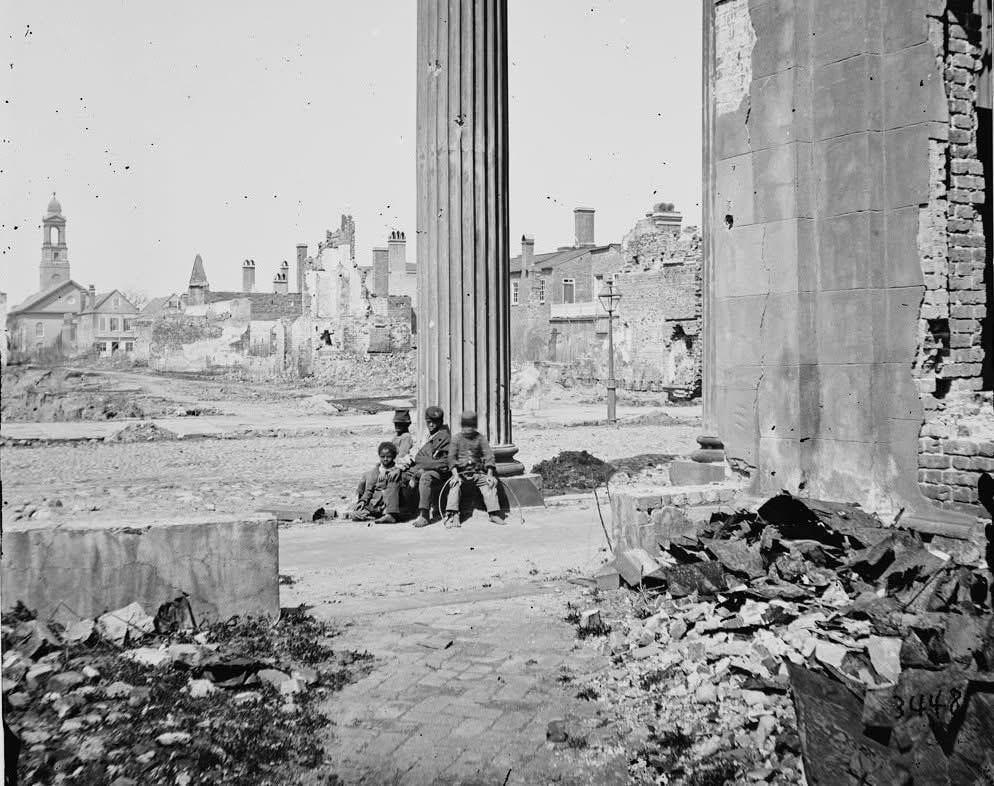 Children sit at the base of a pillar of the Circular Church on Meeting Street in Charleston, SC ca April 1865. [994×776]