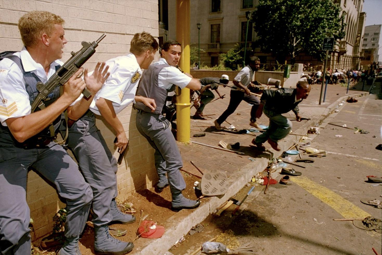 South African Police officers prepare a response to random gunfire as IFP protesters flee during what would become known as the Shell House massacre. 28 March 1994, South Africa [1469×980]