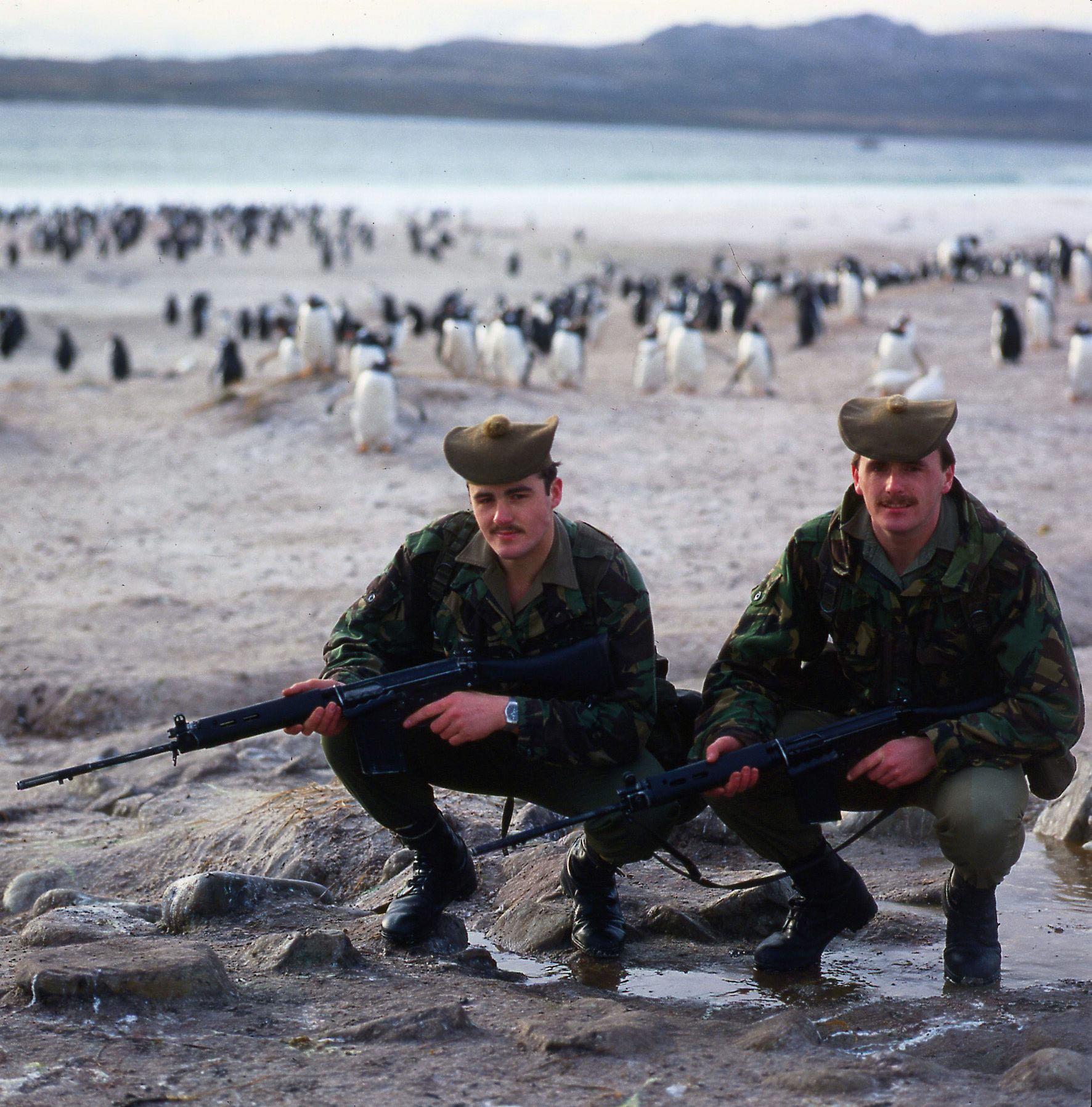 Scottish soldiers who formed part of the garrison left to guard the Falkland Islands after the Falklands War posing with penguins on a beach. (1982) [1772×1796]