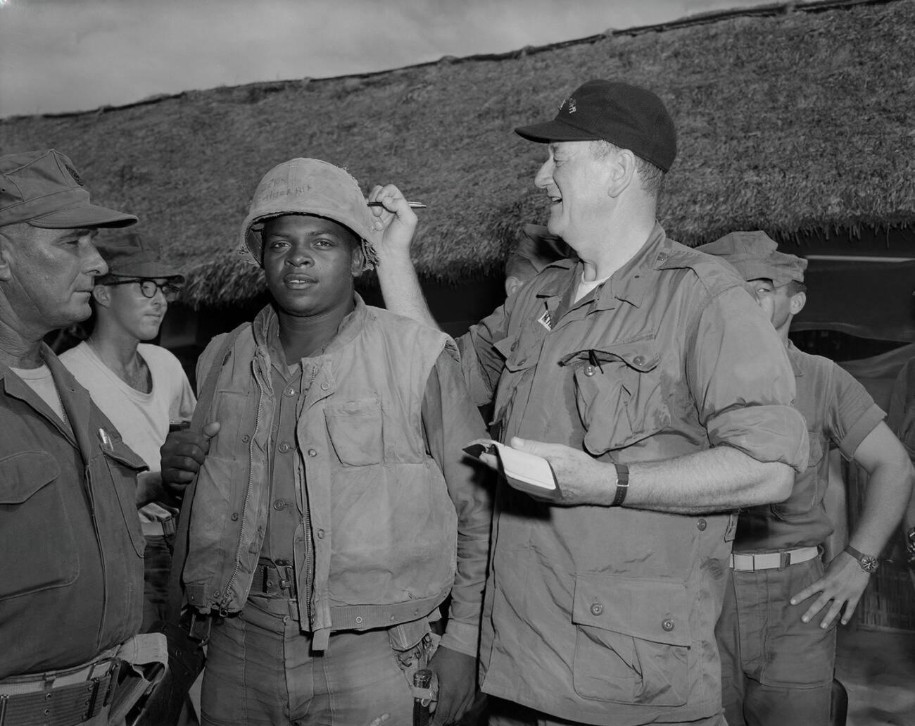 John Wayne signs Private First Class Fonsell Wofford’s helmet during his visit to the 3rd Battalion, 7th Marines, at Chu Lai, Vietnam. (06/20/1966) [1300×1031]