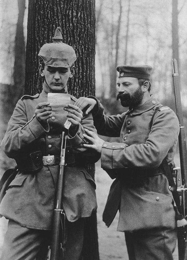 Father and son from the same German regiment read a letter from their respective wife and mother at the front, 1915. [737×1024]
