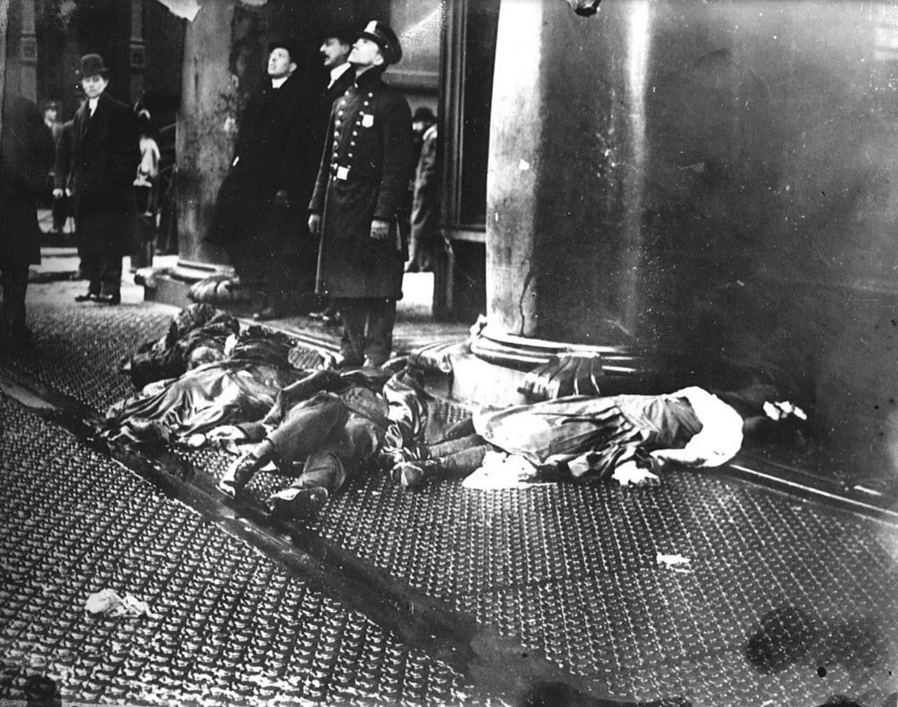 March 25th, 1911, bystanders look up at the burning Triangle Shirtwaist Factory next to the bodies of those who jumped to escape the flames [1284X1011].