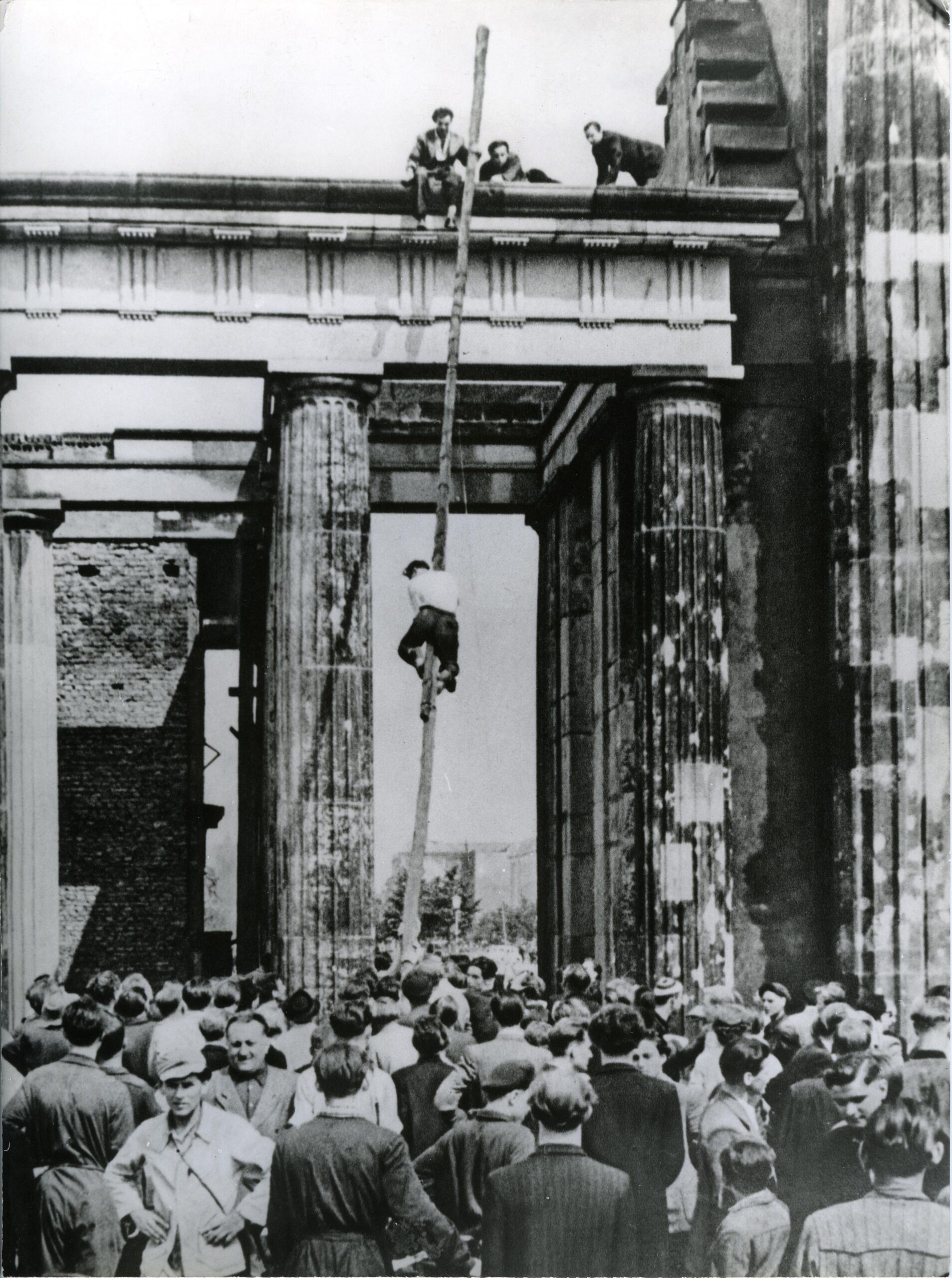 A citizen climbing a pole to lower the red flag flying over the Brandenburg Gate during the 1953 East German uprising [4050 x 5435]