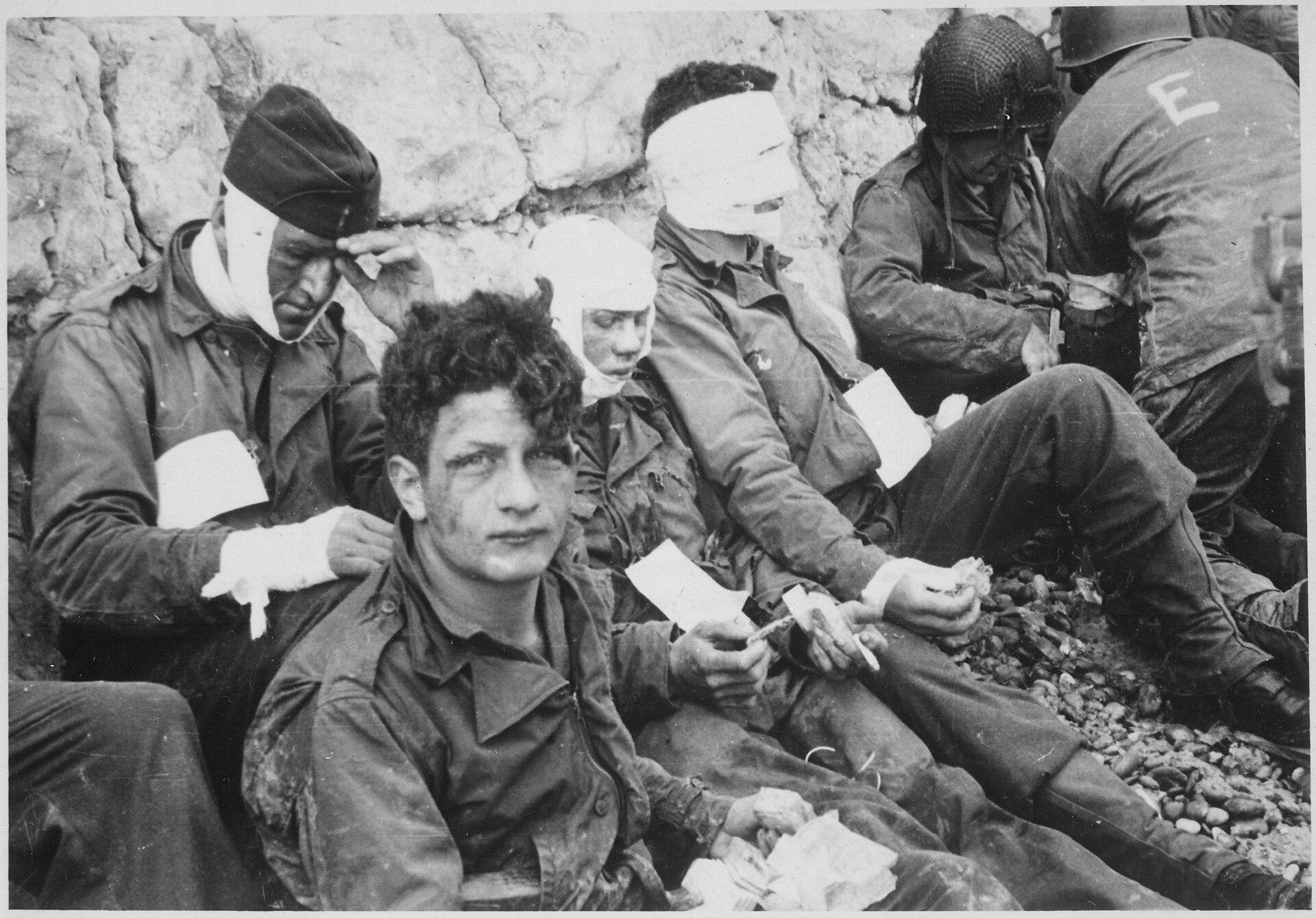 American soldiers of the 16th Infantry Regiment, injured while storming Omaha Beach on D-Day, wait by the Chalk Cliffs for evacuation to a field hospital for further medical treatment. Normandy, 6 June 1944 [3000 × 2092]