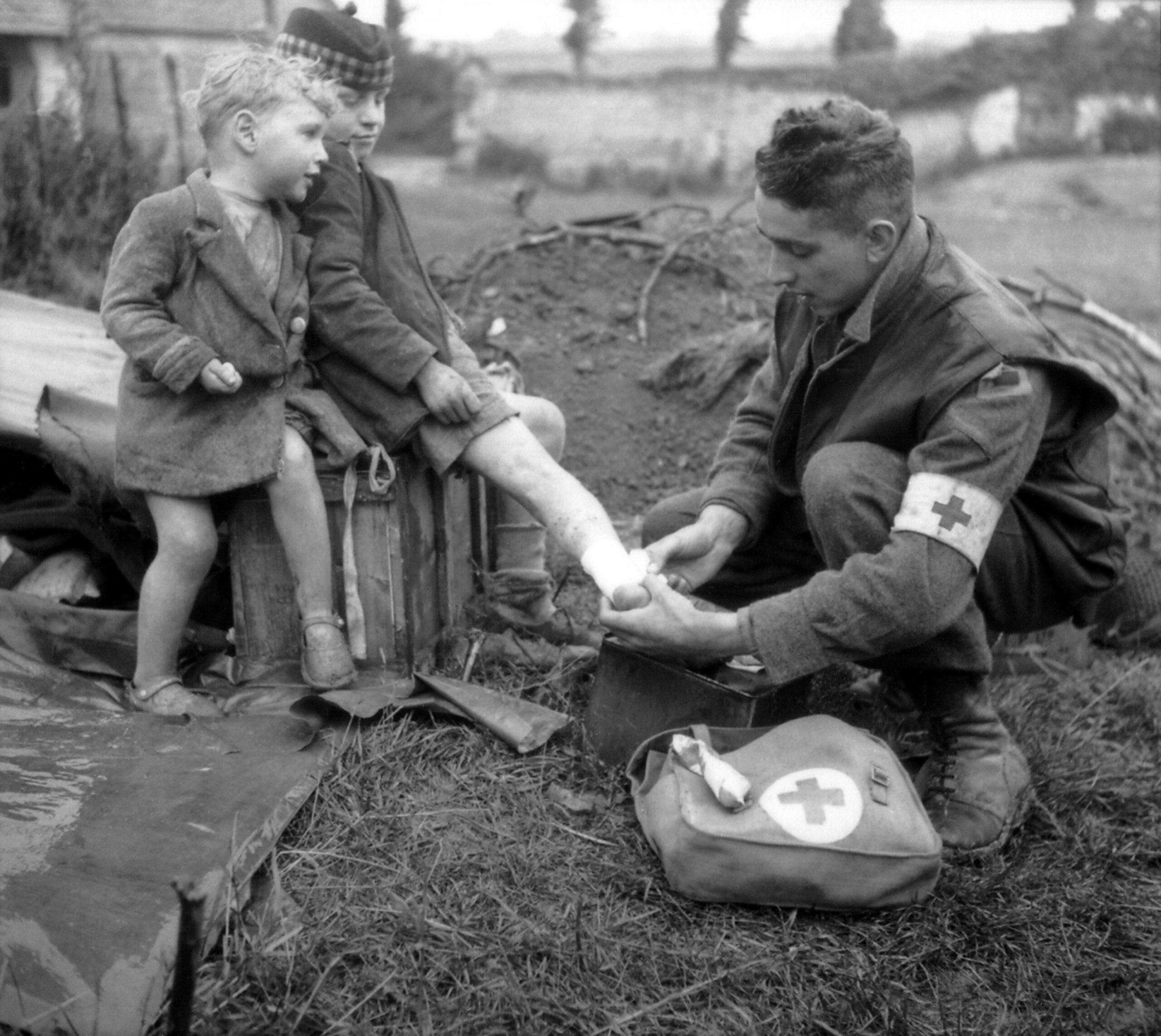 A Royal Canadian Army Medic bandages the burnt leg of a French boy as his brother looks on. Taken in Villons-les-Buissons, France during the Battle of Normandy. 19 June 1944 [3044 × 2717]