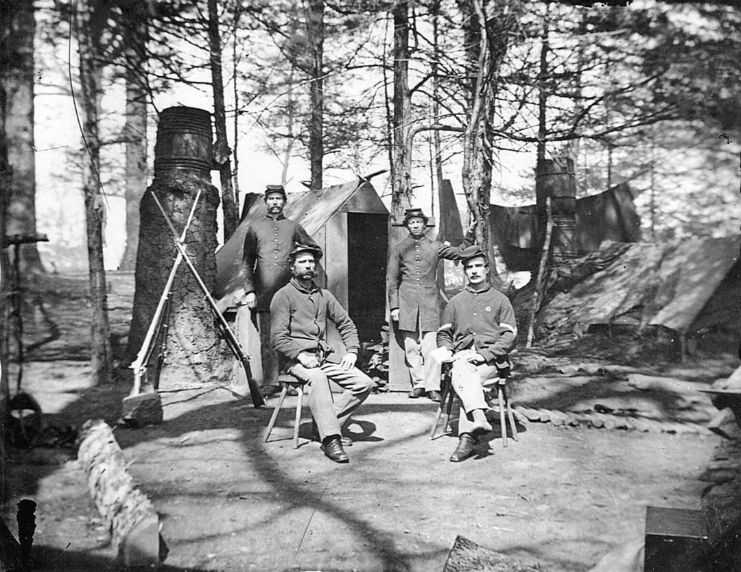 Billy Yanks pose proudly in front of their rudimentary shelter. Note the barrels used as chimneys and the log path used to avoid mud during heavy rains. Petersburg Campaign, 1864. [1080×834]
