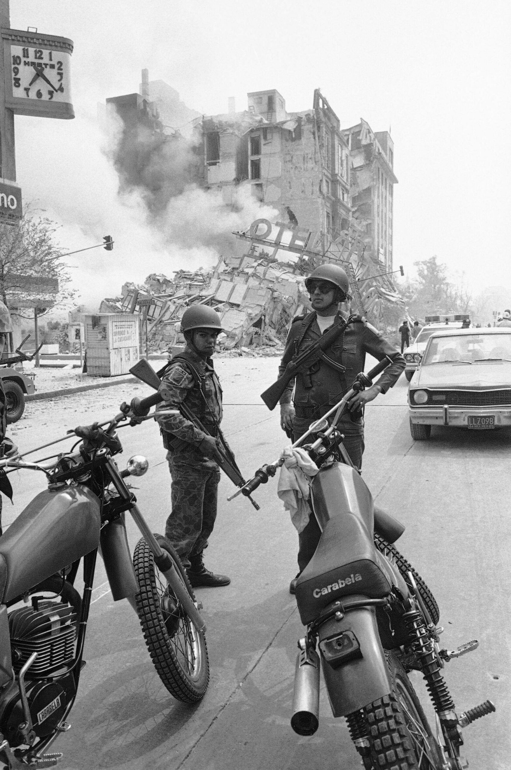 Mexican Army soldiers standing guard amid the rubble in Mexico City after a devastating 7.8 earthquake hit the city. The clock on the left is stopped at the moment the earthquake struck. (1985) [1991×3000]