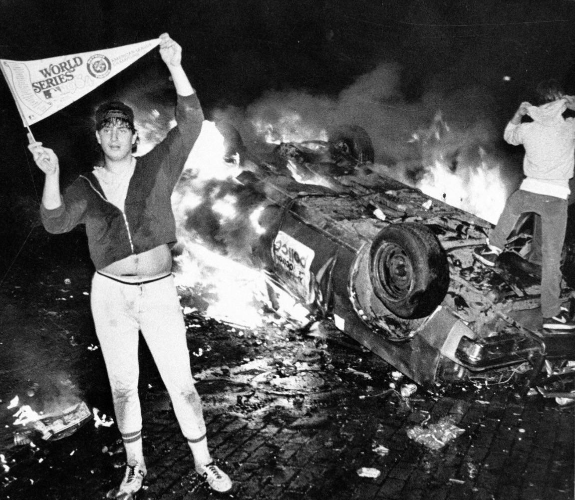 Detroit Tigers fan posing beside an overturned burning police car after the Tigers won the World Series, Detroit, Michigan, October 1984 [1152×1002]