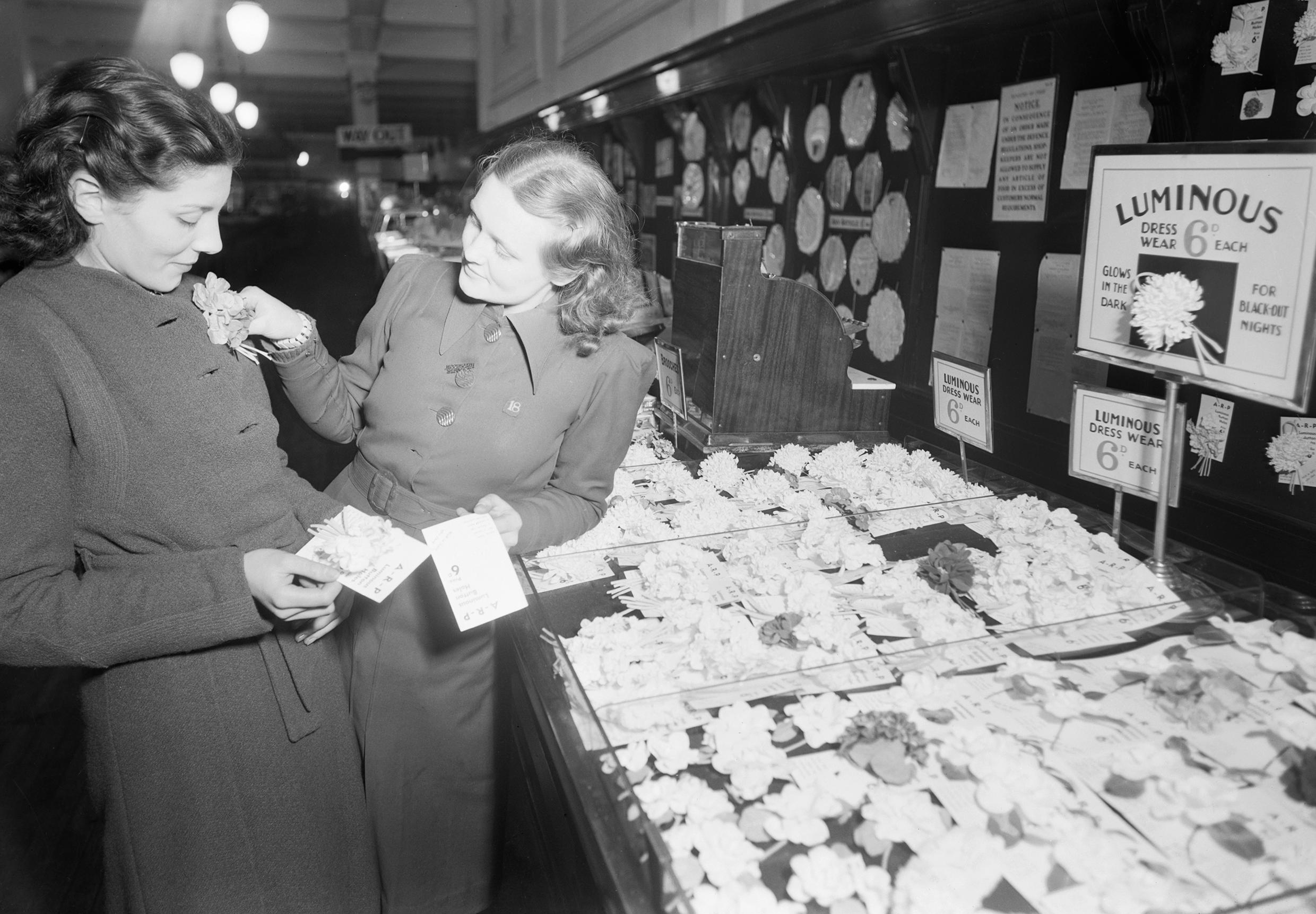 A shop assistant shows a customer a luminous flower in Selfridge’s department store, London. The flowers were designed to glow in the dark during wartime blackouts, helping people navigate streets safely amid enforced darkness. (1940) [2480×1724]