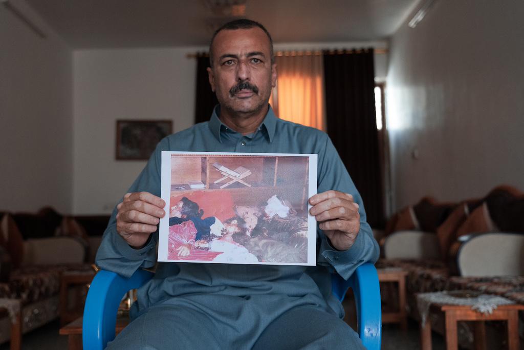 Raseef holds up a photo of the bodies of his relatives, Ayda Yassin Ahmed and four of her children after they were executed by US Marines in Haditha. Only one daughter, Safa, 11, survived. November 19, 2005. [1024 × 683]