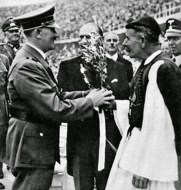 Spyridon Louis, winner of the marathon at the inaugural modern Olympic Games in Athens, presents an olive branch to Adolf Hitler during the opening ceremony of the Summer Olympics in Berlin (1936) [702 × 737]