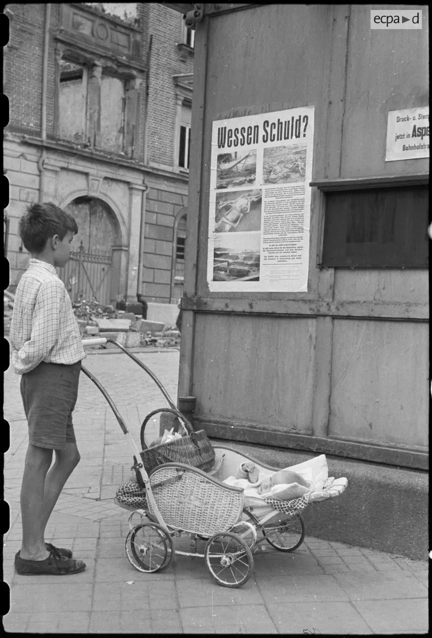 June 1945: In French-occupied Stuttgart, Germany, a boy looks at a poster with photos of holocaust victims, entitled “Whose Fault?” [866×1280]