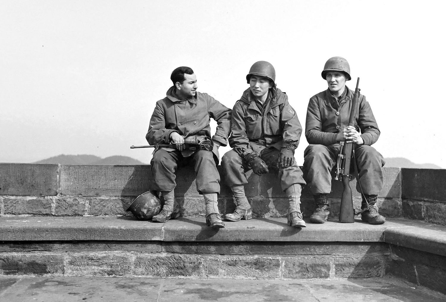 Three U.S. Army soldiers sit together in Dossenheim, France, as their units prepare to move east, into Germany. From left: Private David Taub, T/5 Shigeo Takayama, and an unidentified soldier. February of 1945 [1500 × 1015]