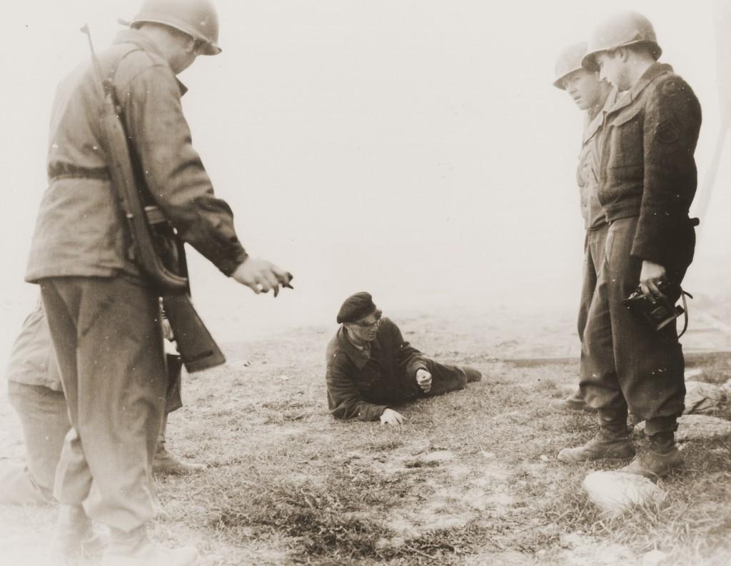 Bonde Gaza, a Hungarian musician who survived the Gardelegen massacre where over 1,000 slave laborers were burnt alive, demonstrates to American soldiers how he managed to escape from the barn which the SS had set on fire. Germany, April 14–18, 1945, [1024 × 793].