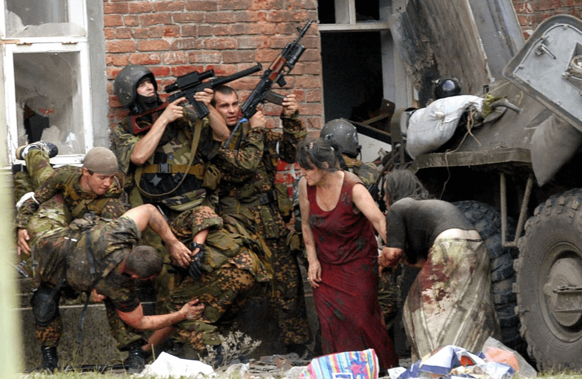 Russian special forces storm Beslan School No. 1 after Chechen extremists seized more than 1,100 hostages inside, while injured hostages take cover nearby. Explosions, fire, and the ensuing firefight killed 334 hostages, including 186 children. Beslan, North Ossetia. September 3, 2004. [1135×739]