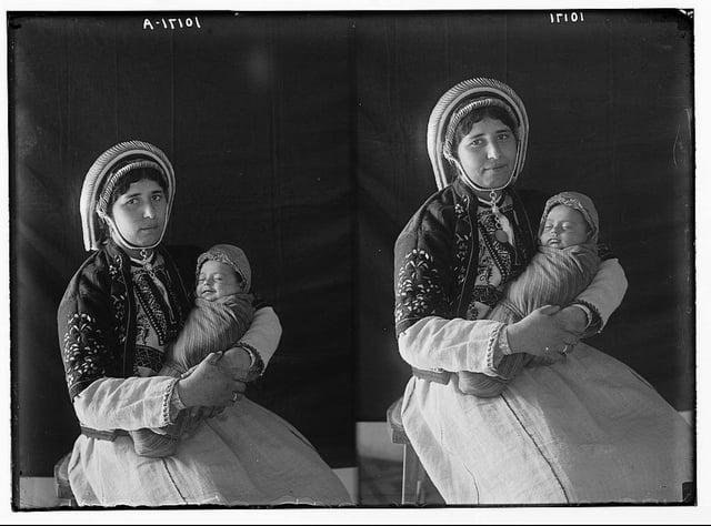 A Palestinian woman of Ramallah in traditional embroidered dress and cradling a baby, 1934 [640×480]
