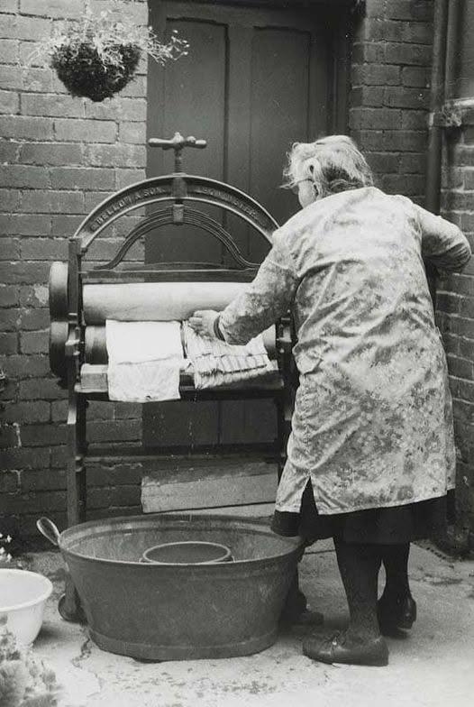 Mrs. Bennett using a cast iron mangle to squeeze water out of wet laundry. Abbey-cwm-hir, Wales, 1960s.  [526×724]