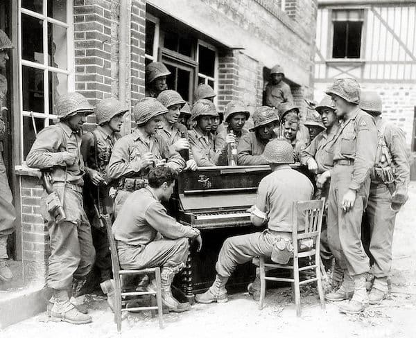 A group of American soldiers has gathered around a piano and sings a song in the street Montéglise. 10th August 1944. The two GI’s on the right wear the insignia of the U.S. Army’s 2nd Armored Division, which has just arrived in Barenton, Normandy, France.  [600×488]