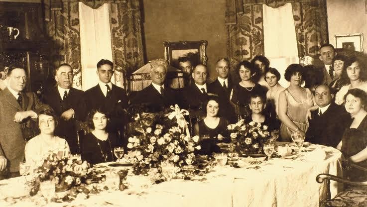 One of George Remus lavish dinner parties at his Price Hill home, 1920s. Remus is seated with his wife, Imogene, standing to his right, and his daughter with her arm on Remus’ shoulder. Remus will murder his wife in 1927.[737×416]