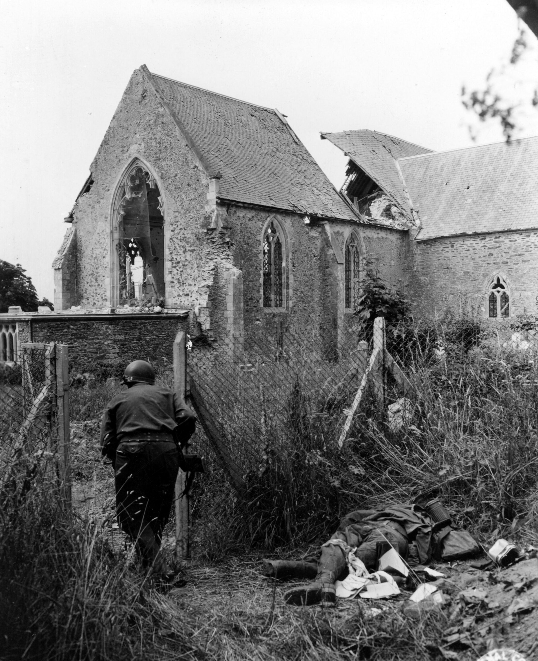 A U.S. soldier from the 29th Infantry Division advances past a dead German soldier toward the wrecked Église Saint-Georges de Saint-Georges-Montcocq in Saint-Lô, Normandy, France. 23 July 1944 [4230 × 5199]