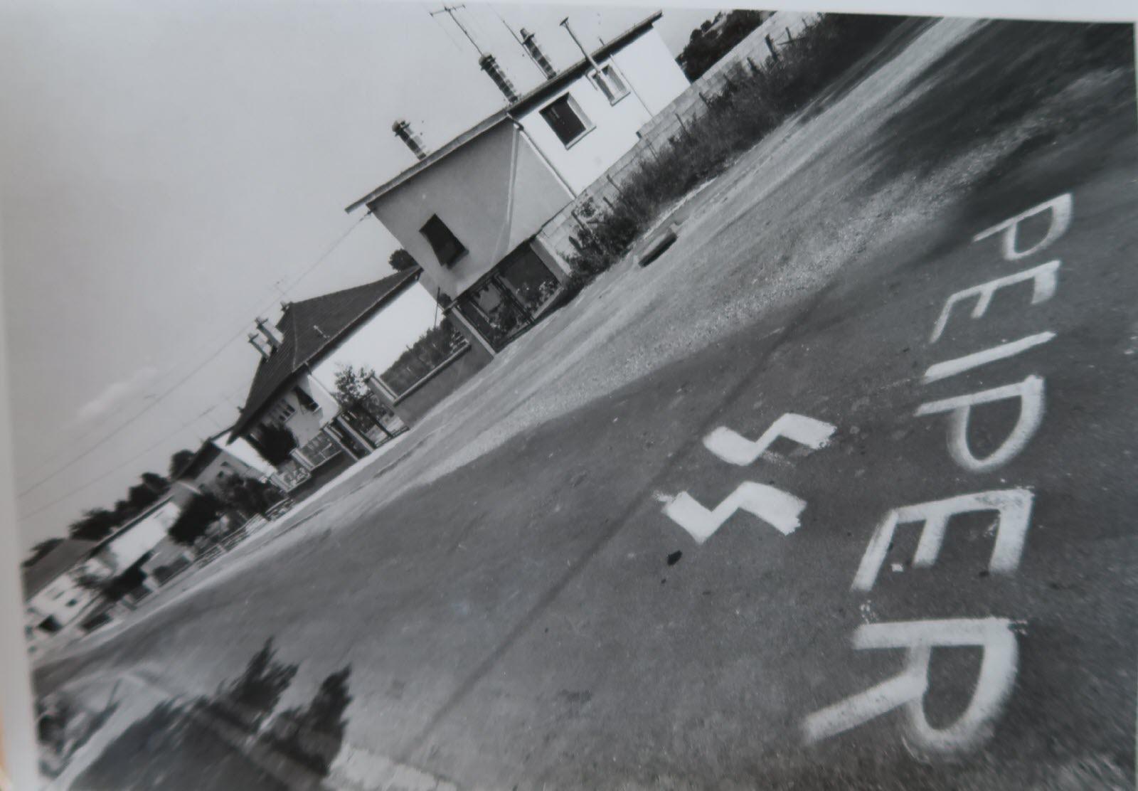 Graffiti on the road marking the house where former SS officer and convicted war criminal Joachim Peiper lived after settling in Traves, France. In July 1976, Peiper’s house was firebombed by French Communists, and an unidentified burned body was found clutching a pistol. [1600 × 1112].