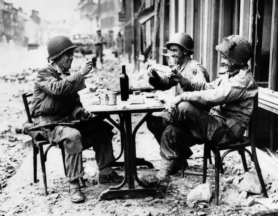 An American version of a sidewalk cafe, in fallen La Haye du Puits, France on July 15, 1944, as Robert McCurty, left, from Newark, New Jersey, Sgt. Harold Smith, of Brush Creek, Tennessee, and Sgt. Richard Bennett, from Wilkes Barre, Pennsylvania, raise their glasses in a toast. [900×701]
