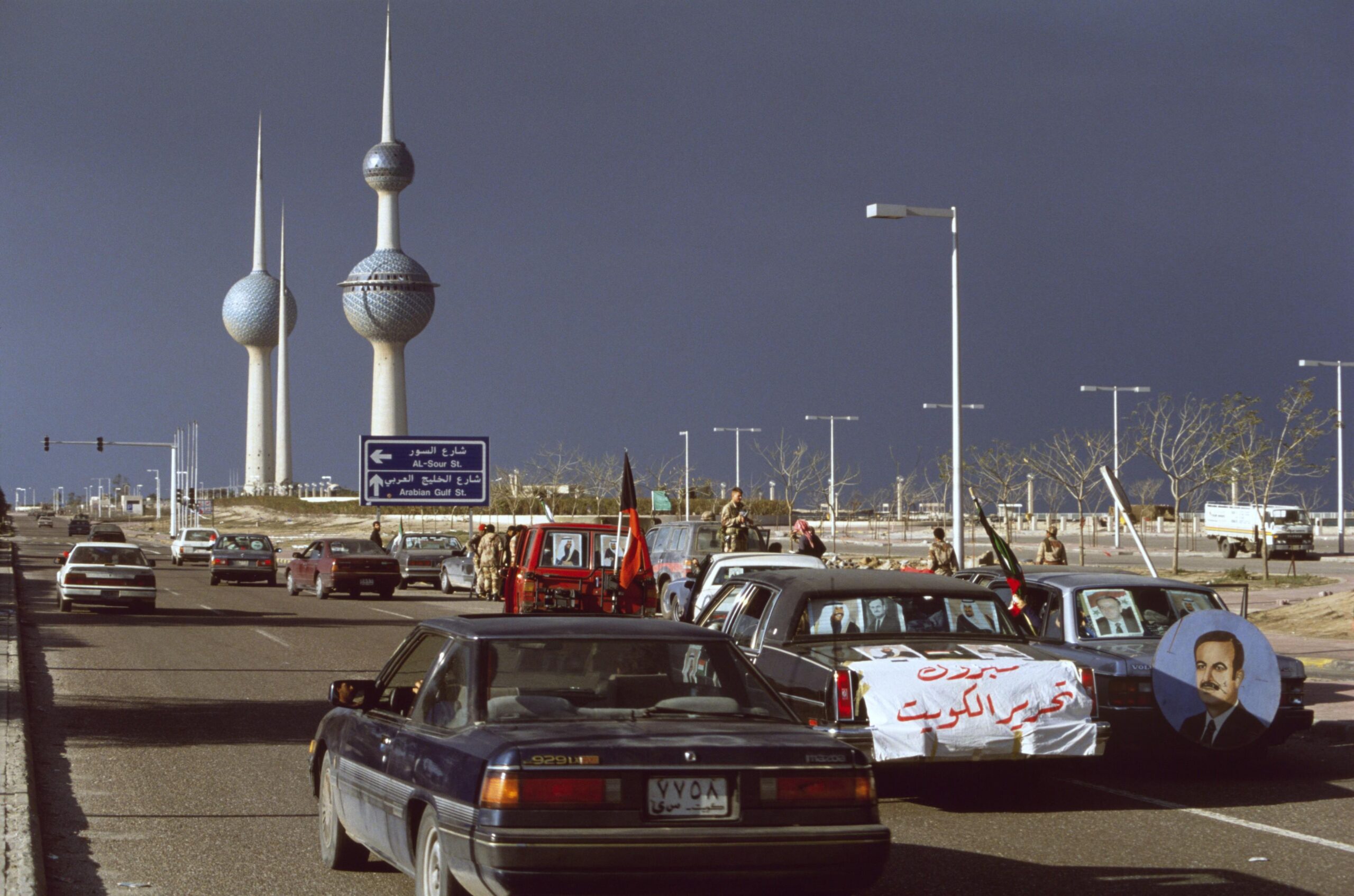 Motorists, south of the iconic Kuwait Water Towers, celebrating the liberation of Kuwait from invading Iraqi forces during the First Gulf War. The white banner reads ‘Congratulations on the liberation of Kuwait.’ (1991) [3500×2318]