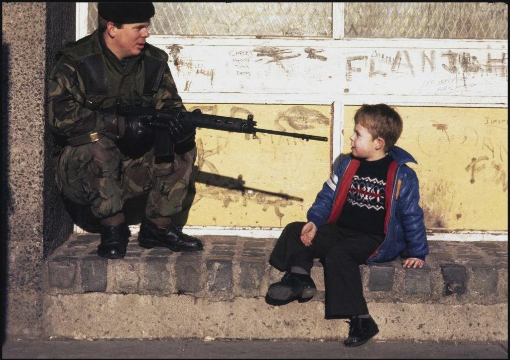 A British soldier talks with a young boy in the republican New Lodge district of Belfast, 20th February 1978. The soldier was about to relieve colleagues in a permanently manned Observation Post in the tower block where the boy lives. [1024×722]
