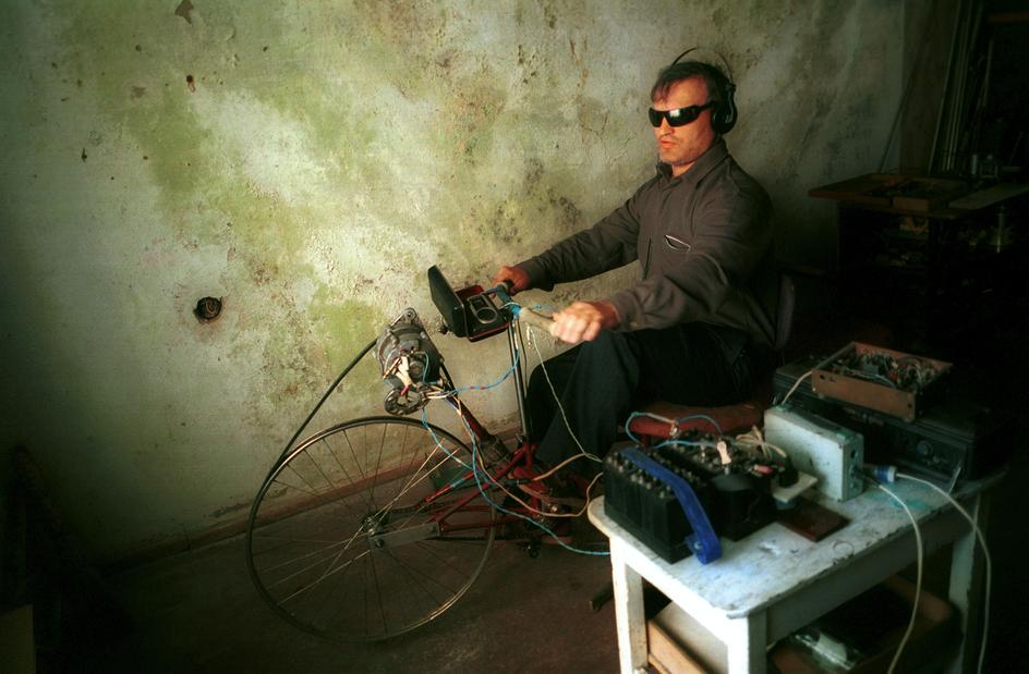 Man generating electricity with a bicycle turned into generator in the House of the Blind, Grozny, March 2002. Dozen of blind people survive in the badly hit shelter by the Russian bombing. They live on 22$ pension. [944×619]